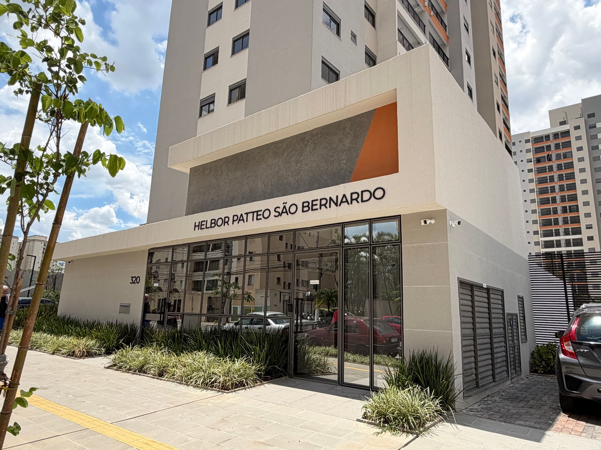 Fachada frontal da portaria e entrada principal do condomínio com paredes de vidro